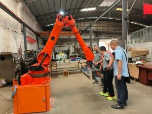 Vietnamese client inspecting 6-axis industrial robotic arm in factory workshop, on-site quality verification for automated material handling
